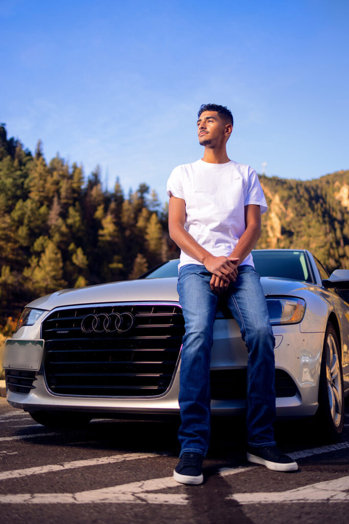 high school senior wearing white shirt and jeans posing by his car in CO
