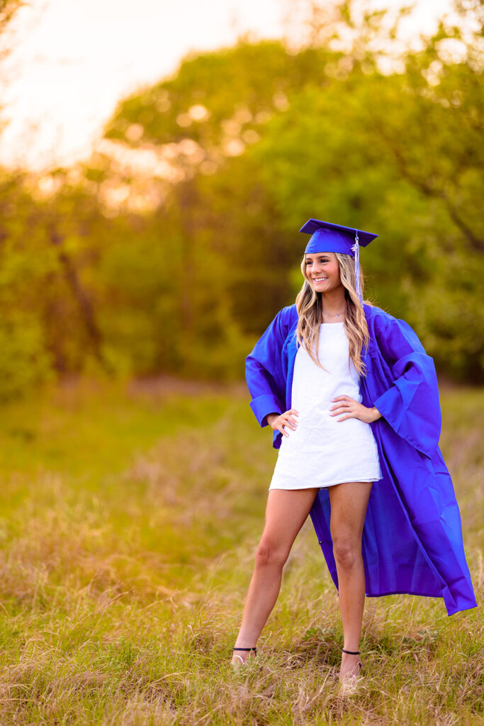 high school senior wearing cap and gown walking through field in CO