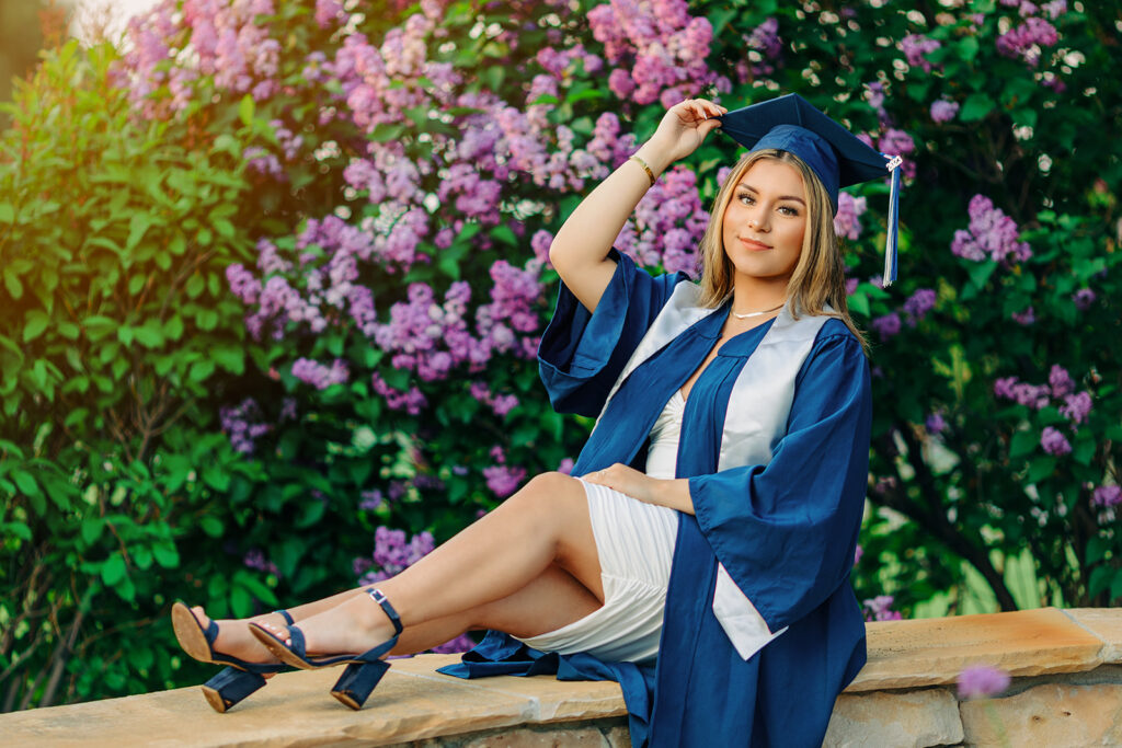 high school senior wearing cap and gown sitting by flowers in CO